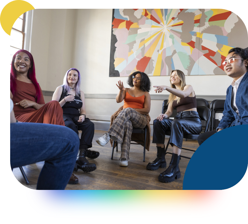 A group of young people sitting in a circle discussing something, smiling. 